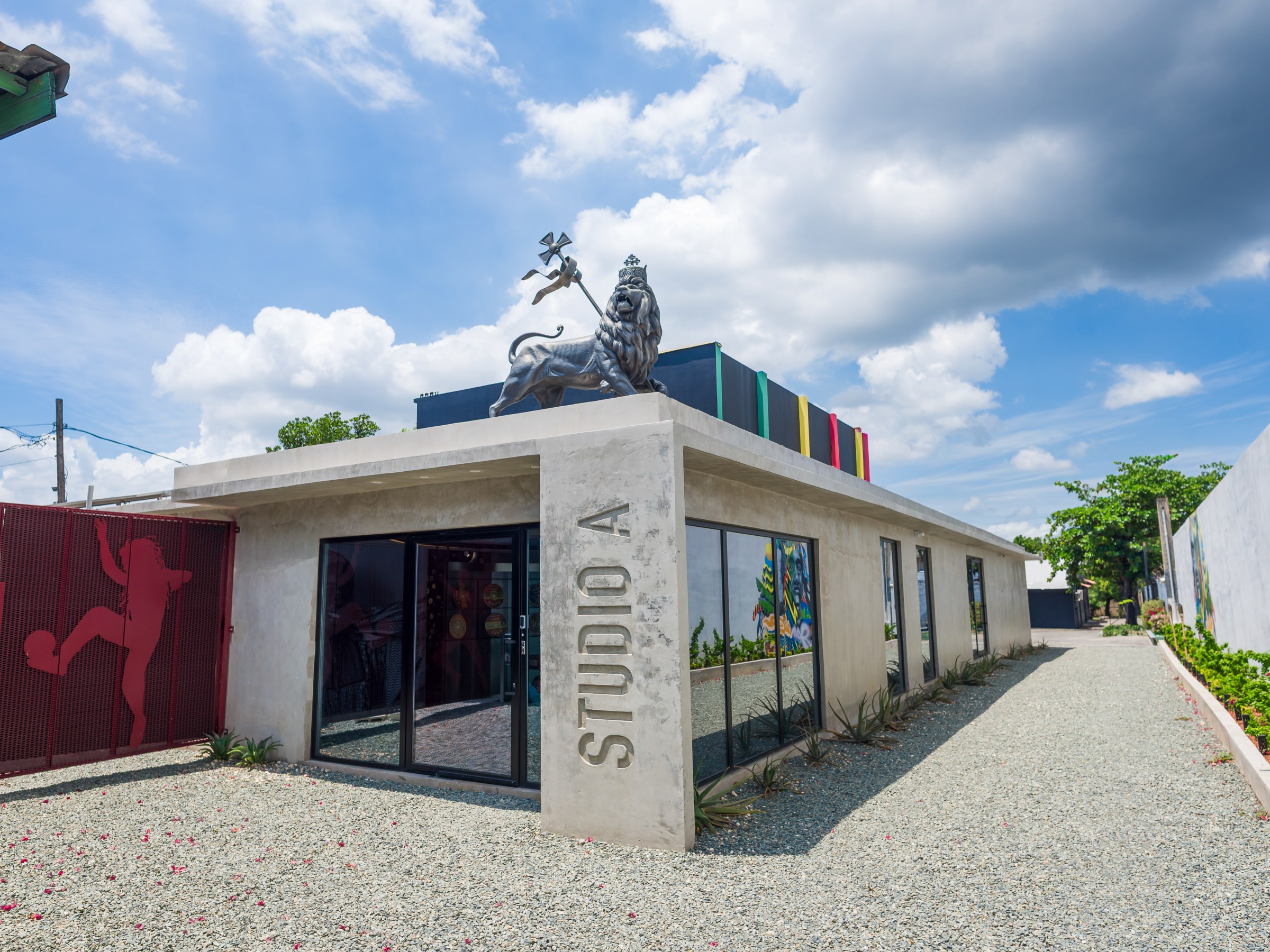 Modern building with 'STUDIO A' sign, gravel path, and rooftop art against a cloudy sky.